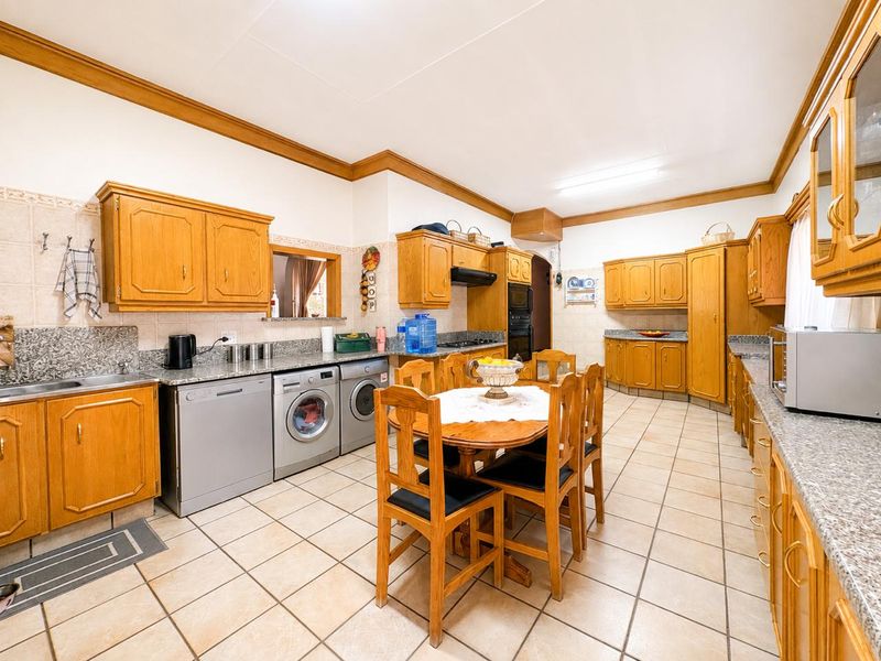 Spacious kitchen featuring extensive wooden cabinetry, granite countertops, built-in oven, and integrated laundry appliances with tiled flooring throughout.