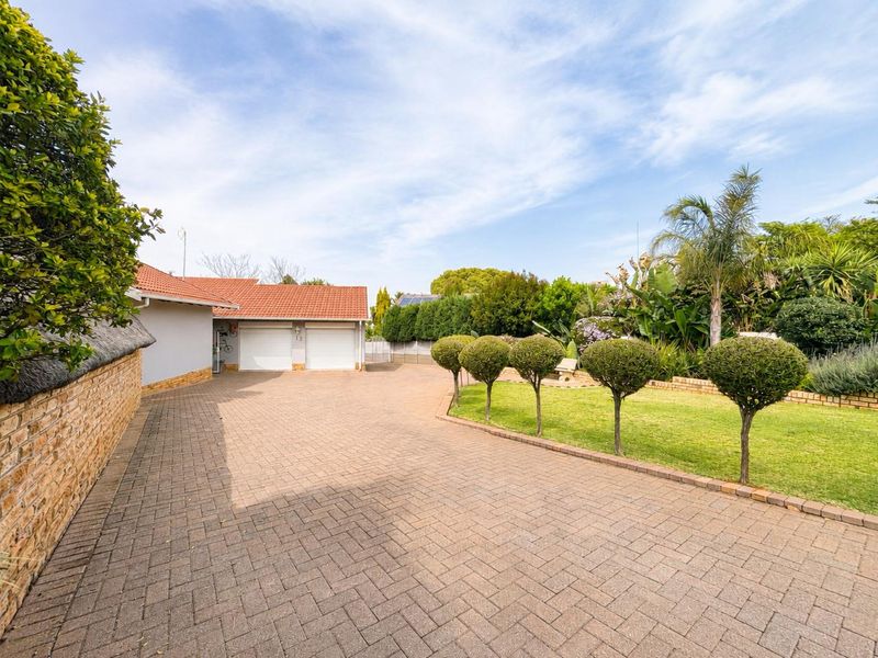Spacious front exterior featuring a paved driveway leading to a double garage, complemented by a well-maintained garden and established landscaping.