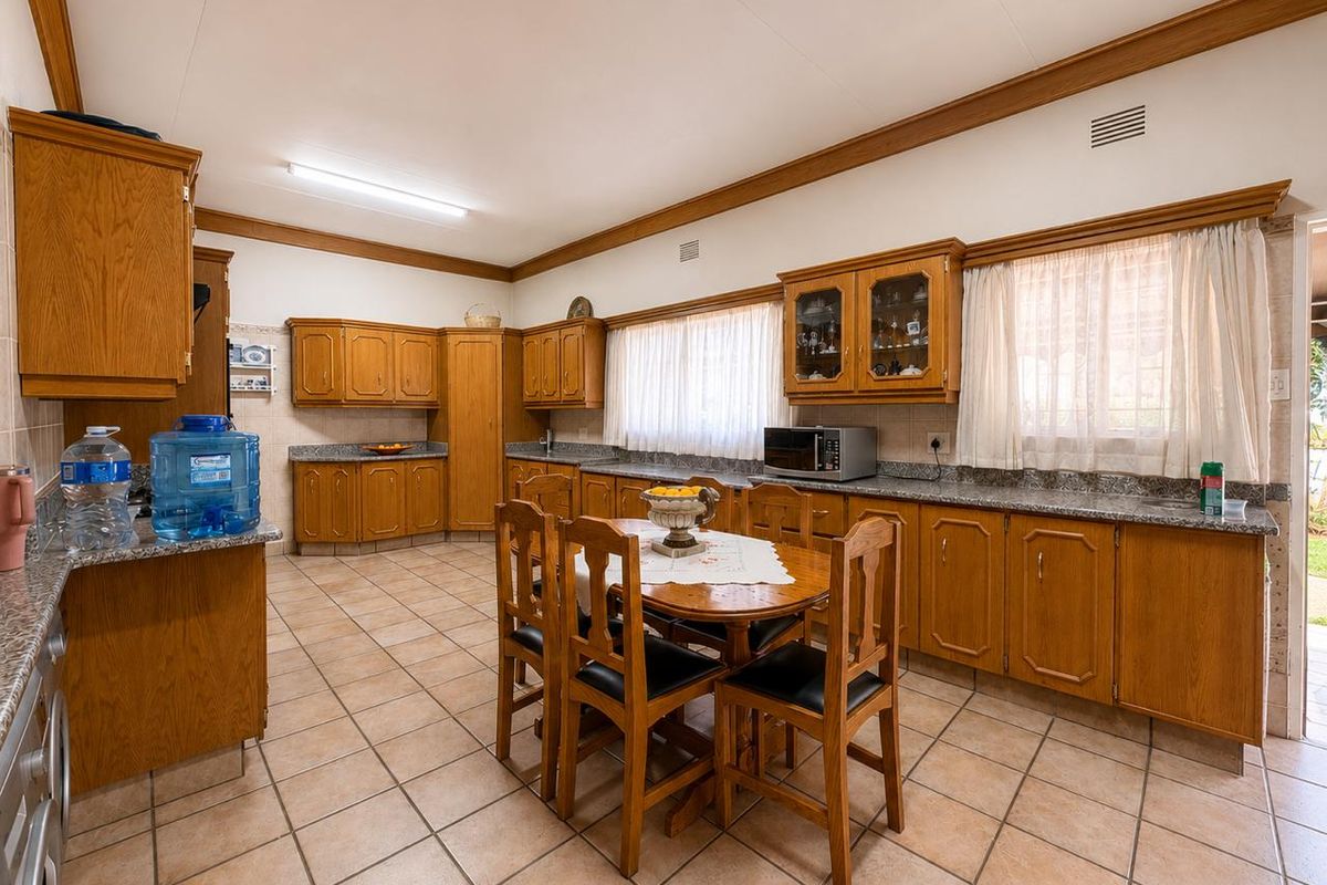 Spacious kitchen featuring extensive wooden cabinetry, granite countertops, tiled flooring, and a central dining area, offering a functional and traditional layout.