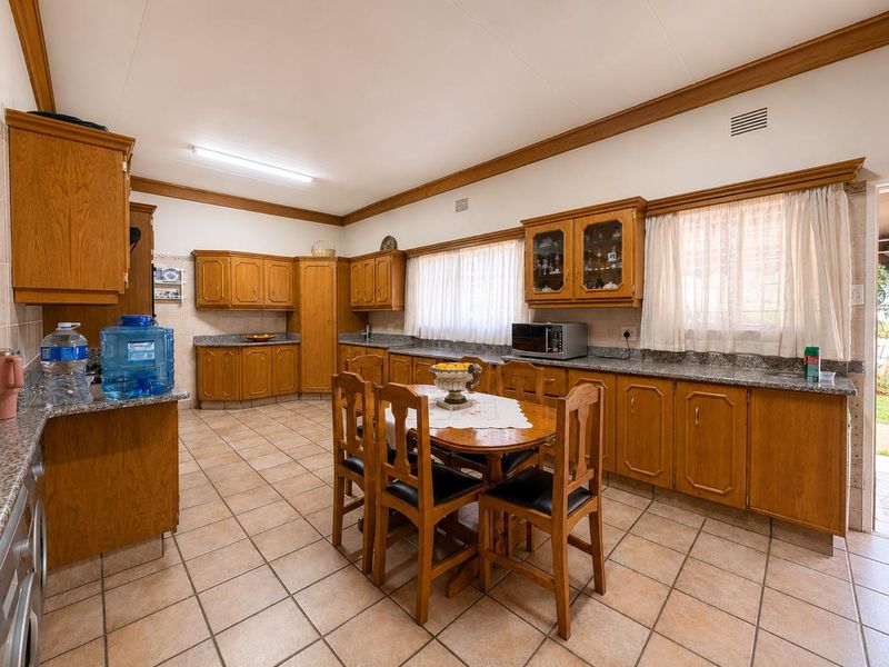 Spacious kitchen featuring extensive wooden cabinetry, granite countertops, tiled flooring, and a central dining area, offering a functional and traditional layout.
