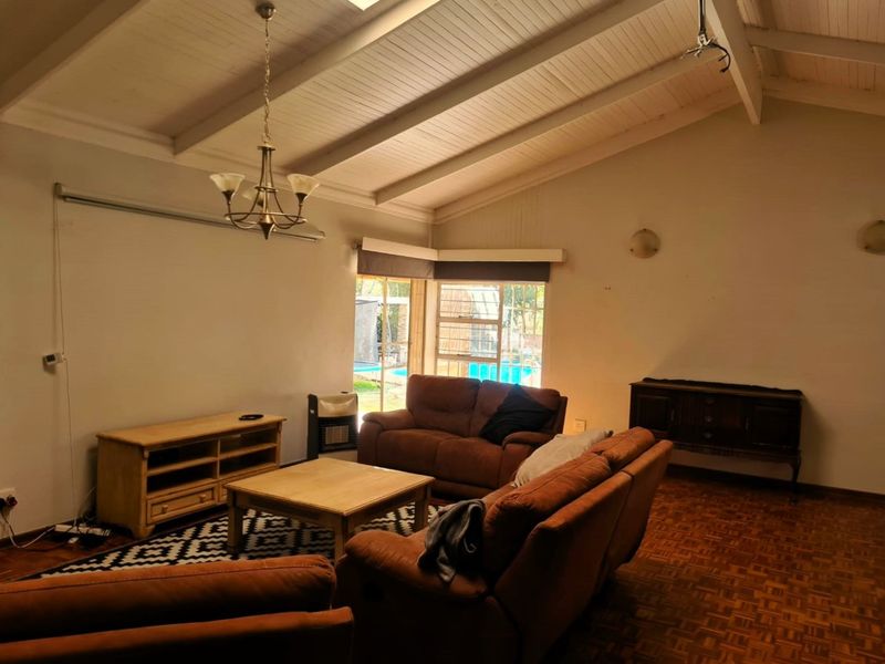 Spacious living room featuring high exposed beam ceilings, classic parquet flooring, and direct access to the outdoor pool area through sliding glass doors.