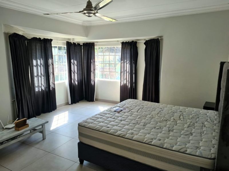 Spacious bedroom featuring tiled flooring, ceiling fan, and large windows with natural light, offering a neutral canvas for personalization.