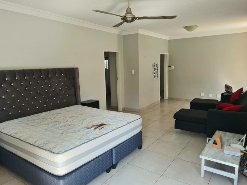 Spacious bedroom featuring neutral wall tones, tiled flooring, coved cornicing, and a ceiling fan, offering a clean and functional living space.
