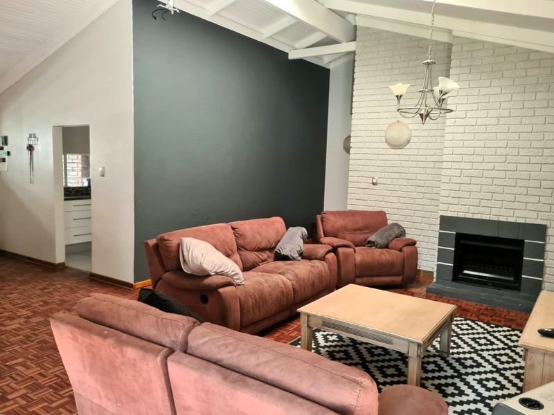Spacious living room featuring a vaulted ceiling with exposed beams, a prominent brick fireplace, and classic parquet flooring.