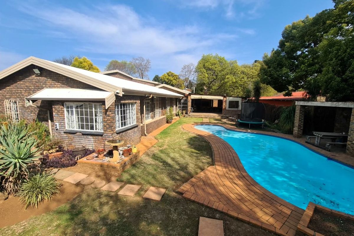 Rear view of the property featuring a brick facade, a swimming pool with brick paving, a well-maintained lawn, and a covered patio area.