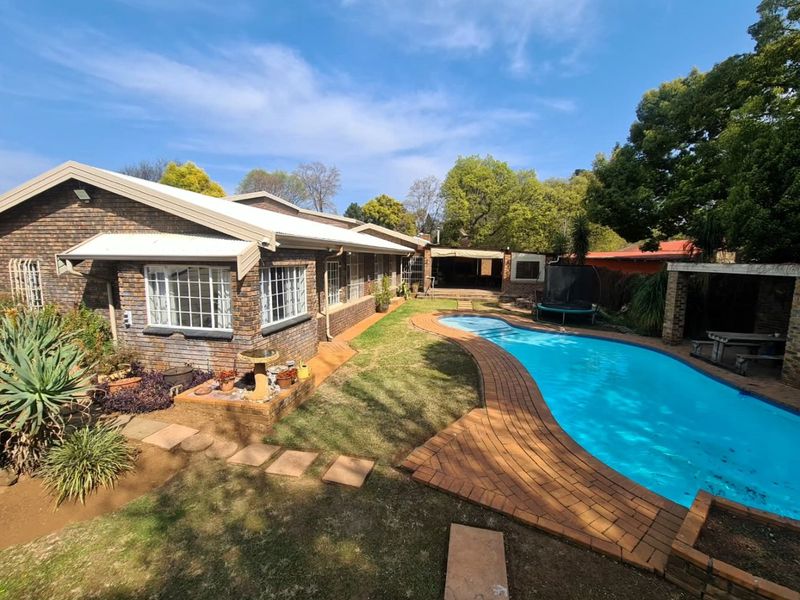 Rear view of the property featuring a brick facade, a swimming pool with brick paving, a well-maintained lawn, and a covered patio area.