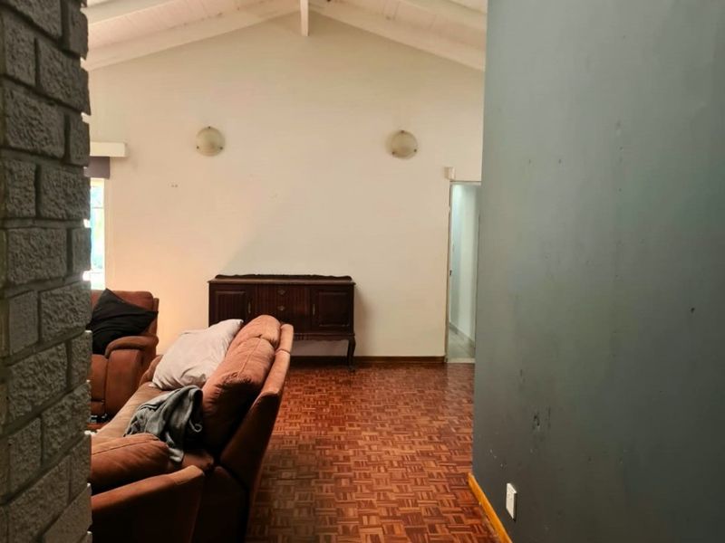 Living room featuring a vaulted ceiling with exposed beams, parquet flooring, and a brick feature wall.