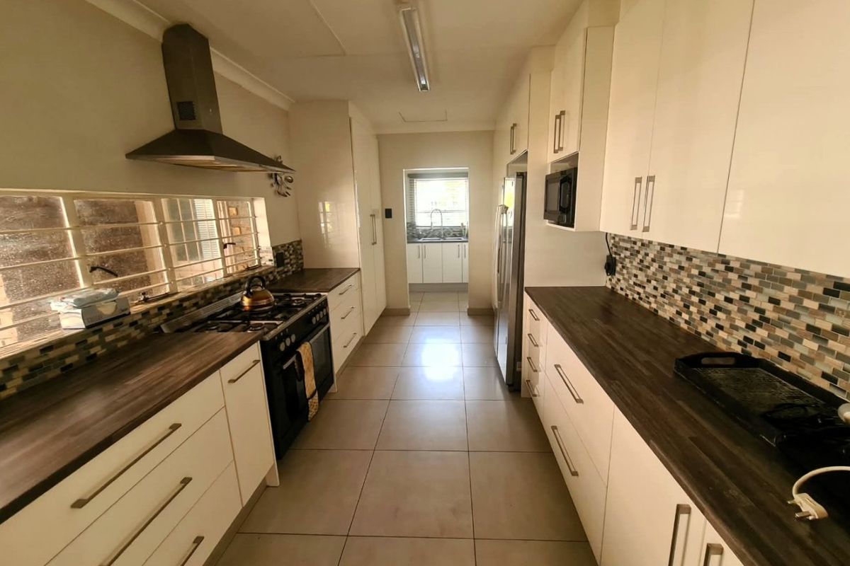 A functional galley-style kitchen featuring white cabinetry, dark laminate countertops, a gas stove with extractor fan, and a mosaic tile backsplash.