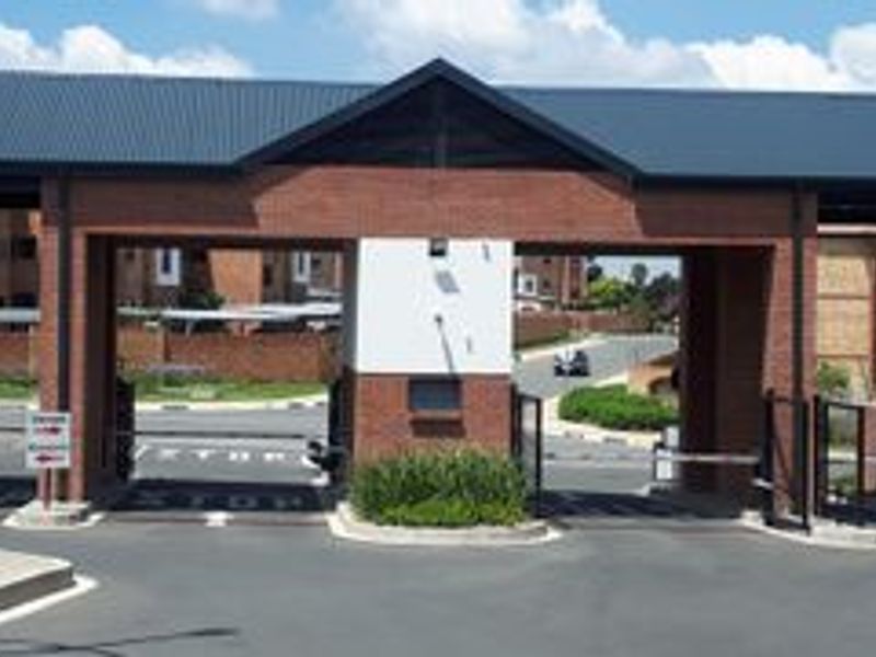 A secure gated entrance to the apartment complex featuring brick pillars, metal roofing, and automated boom gates for controlled access.