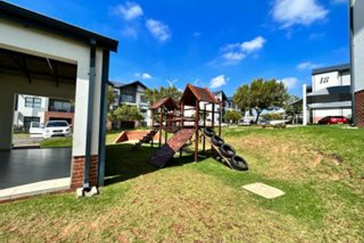 A communal outdoor area featuring a children's playground, well-maintained lawn, and a covered patio space within an apartment complex.