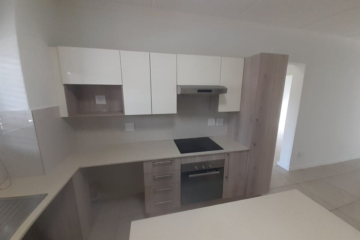Modern kitchen featuring light wood-tone and white cabinetry, stone countertops, integrated electric hob, oven, and extractor fan with tiled flooring.