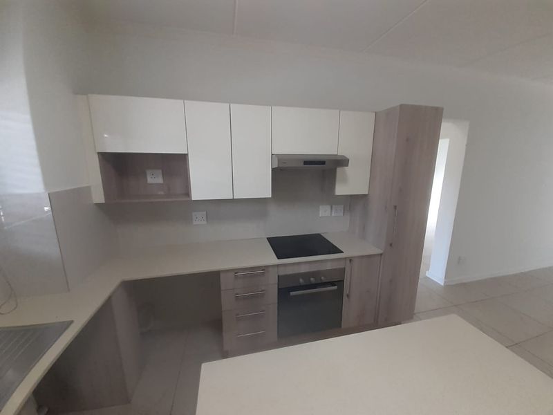 Modern kitchen featuring light wood-tone and white cabinetry, stone countertops, integrated electric hob, oven, and extractor fan with tiled flooring.