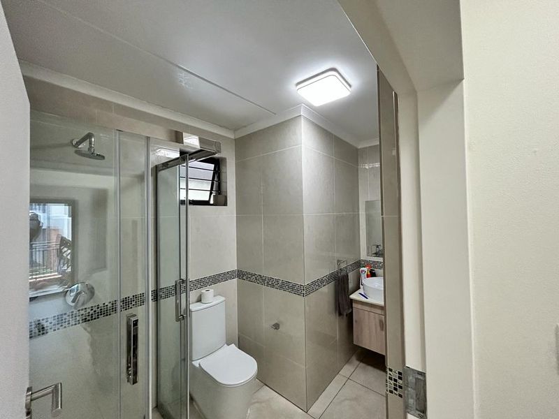 A modern bathroom featuring a glass-enclosed shower, a vanity with a basin, and neutral wall and floor tiling.