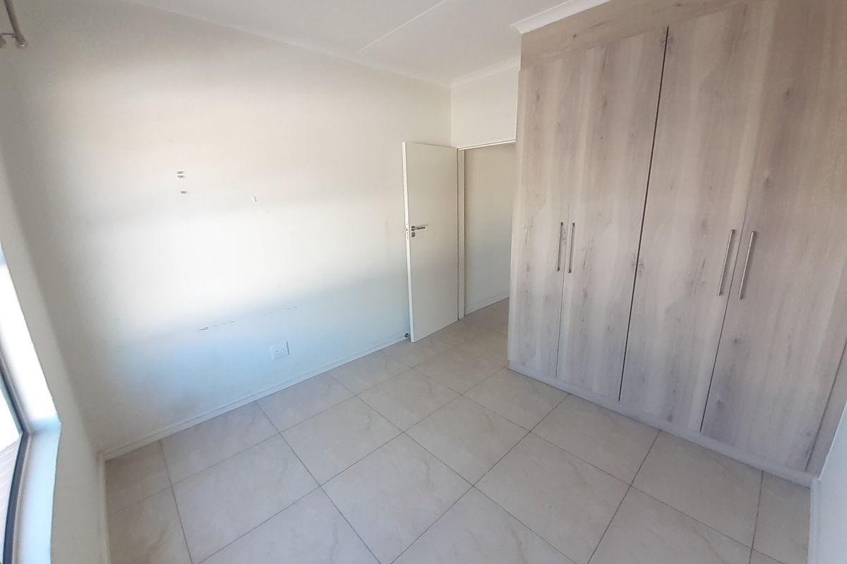 An empty bedroom featuring light-toned built-in cupboards, neutral tiled flooring, and clean white walls, ready for personalization.