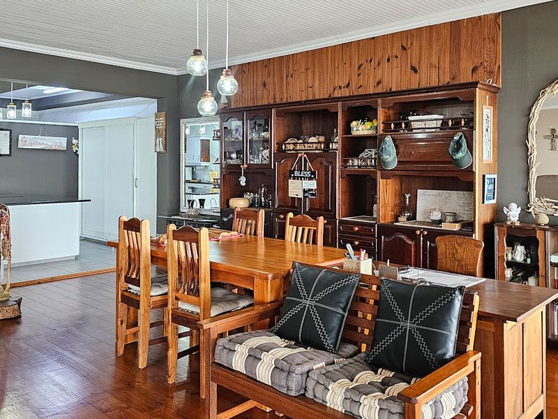Open plan living and dining area featuring timber flooring, beadboard ceiling, and integrated cabinetry, flowing into a kitchen space.
