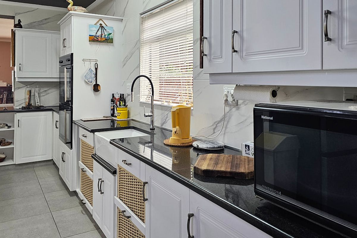 A well-maintained kitchen featuring white cabinetry, dark granite countertops, an apron-front sink, and marble-look wall tiles.