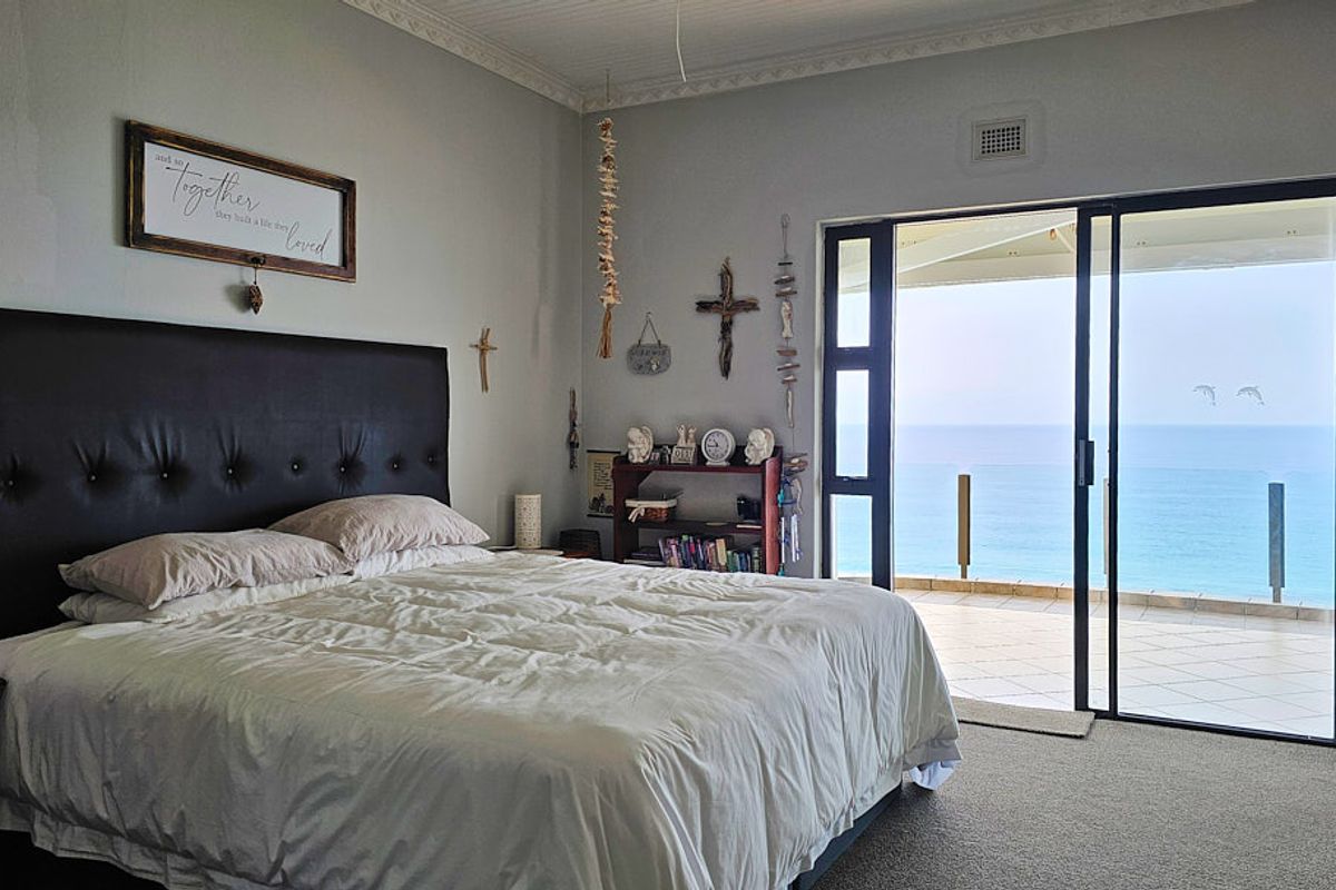 Spacious bedroom featuring carpeted flooring, decorative ceiling cornice, and large sliding glass doors opening onto a balcony with ocean views.