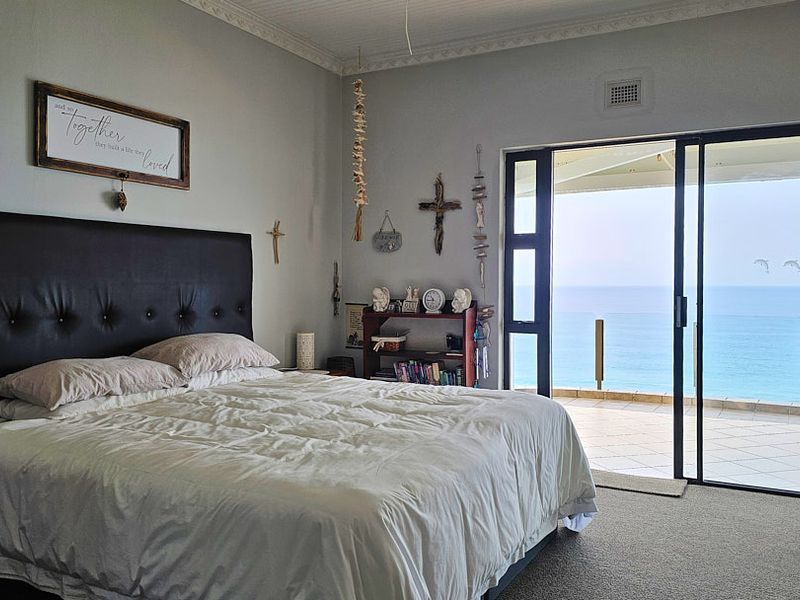Spacious bedroom featuring carpeted flooring, decorative ceiling cornice, and large sliding glass doors opening onto a balcony with ocean views.