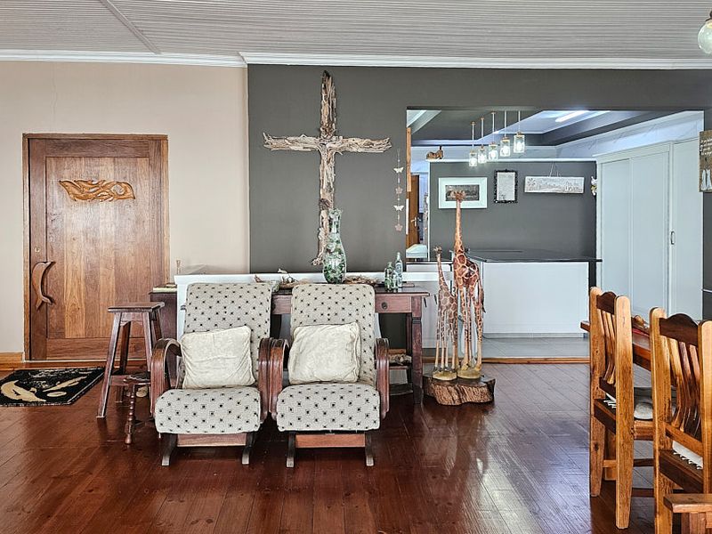 Spacious open-plan living area featuring warm hardwood flooring, a solid timber entrance door, and a seamless transition into the adjacent kitchen space.