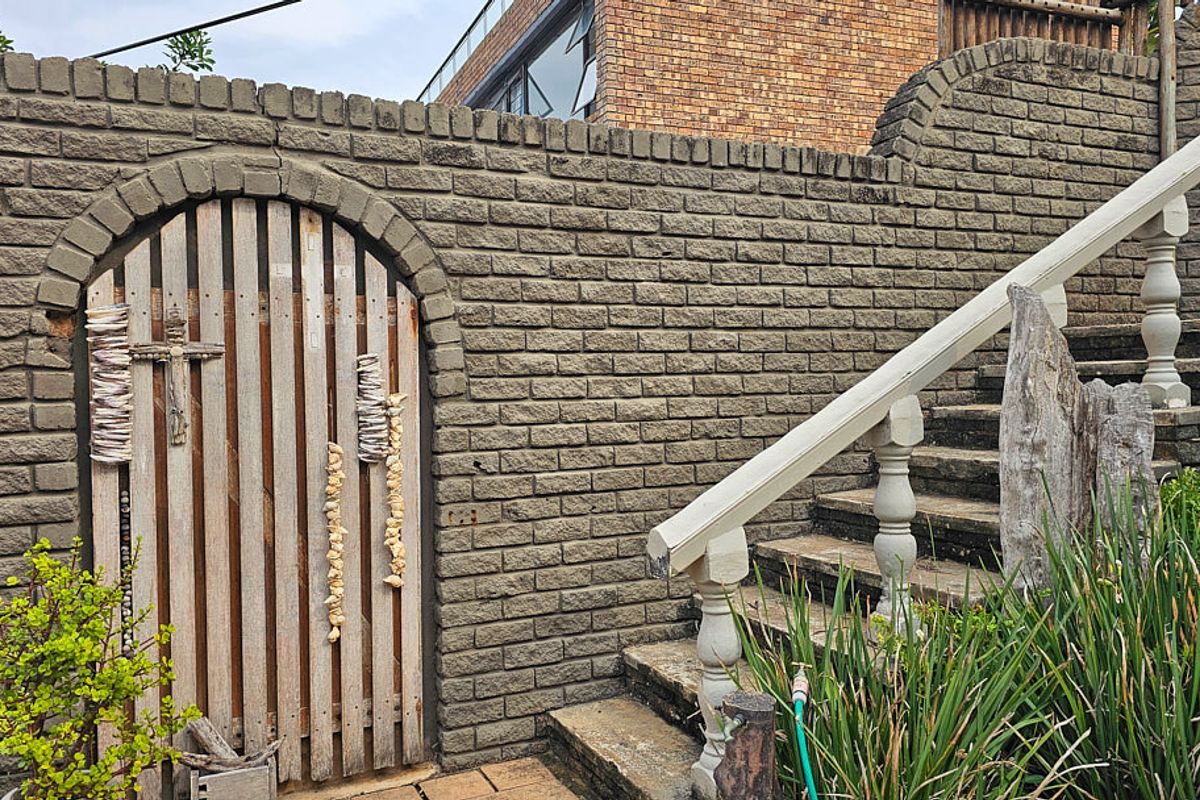Exterior view of a brick boundary wall featuring an arched wooden gate and concrete staircase with a balustrade railing.