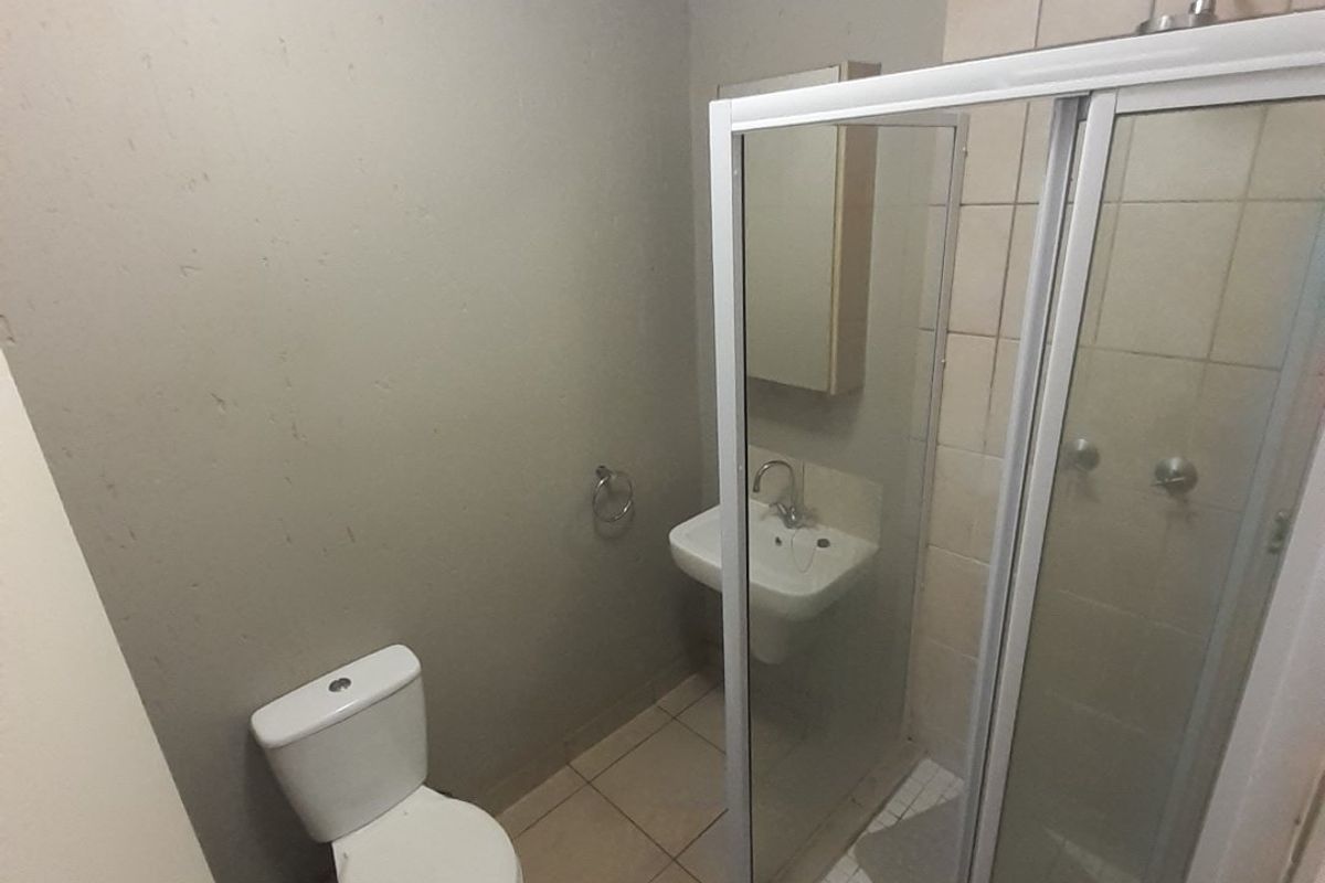 A compact bathroom featuring a shower enclosure, wall-mounted basin, and toilet with tiled flooring and neutral wall finishes.