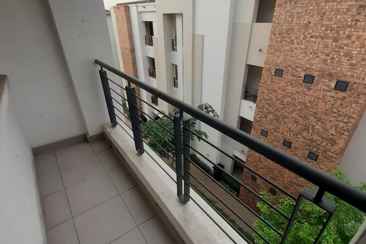 A private apartment balcony featuring tiled flooring and a secure metal balustrade, overlooking the surrounding residential complex.