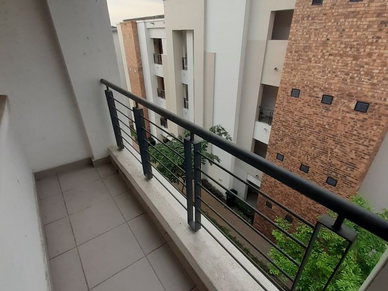 A private apartment balcony featuring tiled flooring and a secure metal balustrade, overlooking the surrounding residential complex.