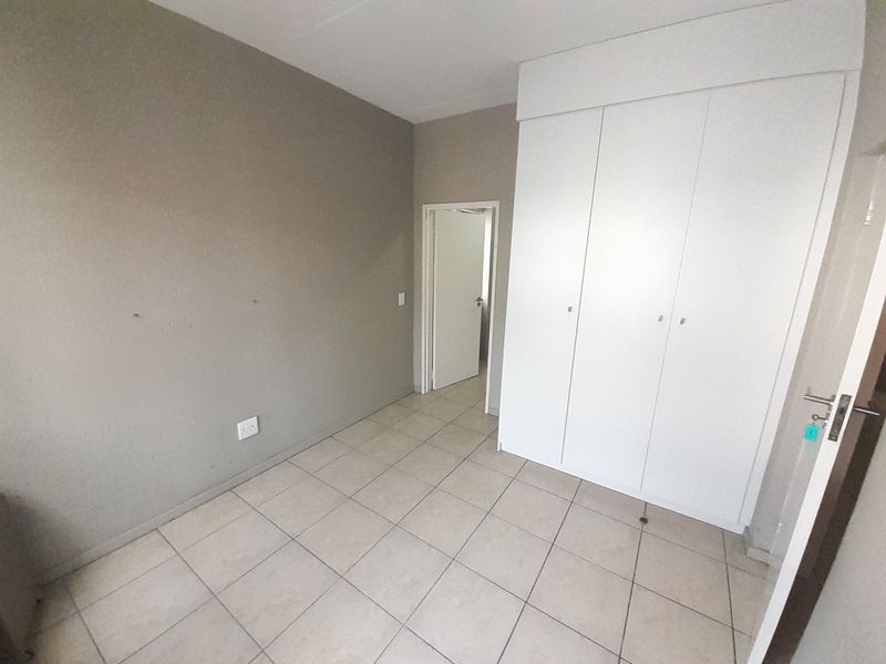 An empty bedroom featuring neutral tiled flooring and white built-in cupboards, offering a clean and versatile space ready for personalization.