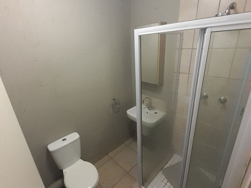 A compact bathroom featuring a shower enclosure, wall-mounted basin, and toilet with tiled flooring and neutral wall finishes.