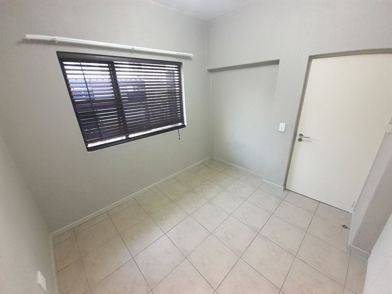 A vacant bedroom featuring neutral tiled flooring, a window with fitted venetian blinds, and a standard internal door.