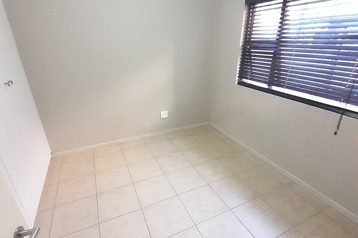 A clean, empty bedroom featuring neutral tiled flooring, a built-in cupboard, and window blinds, offering a versatile space ready for personalization.