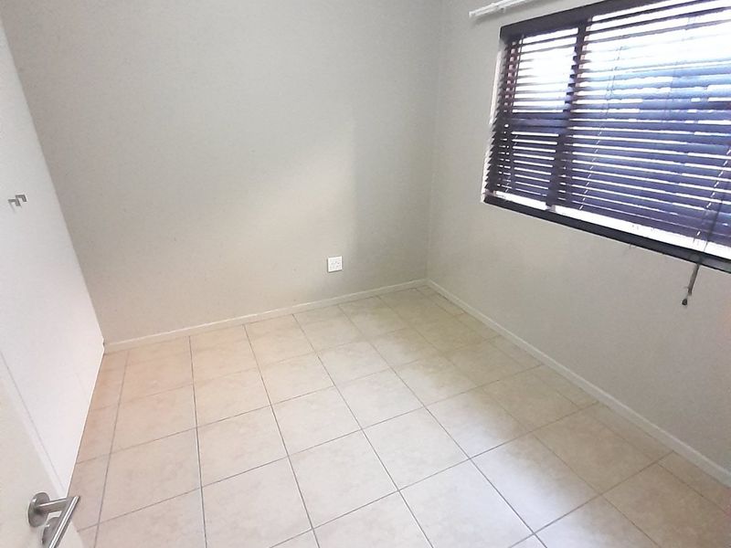 A clean, empty bedroom featuring neutral tiled flooring, a built-in cupboard, and window blinds, offering a versatile space ready for personalization.