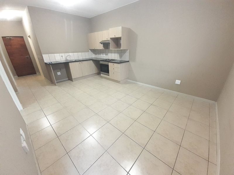 A functional, empty kitchen featuring light-toned built-in cabinetry, laminate countertops, a built-in oven with hob, and neutral tiled flooring.