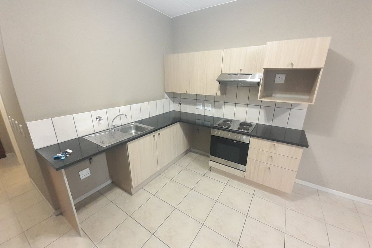 A functional kitchen featuring light wood-finish cabinetry, granite countertops, built-in oven, hob, and extractor fan with neutral tiled flooring.