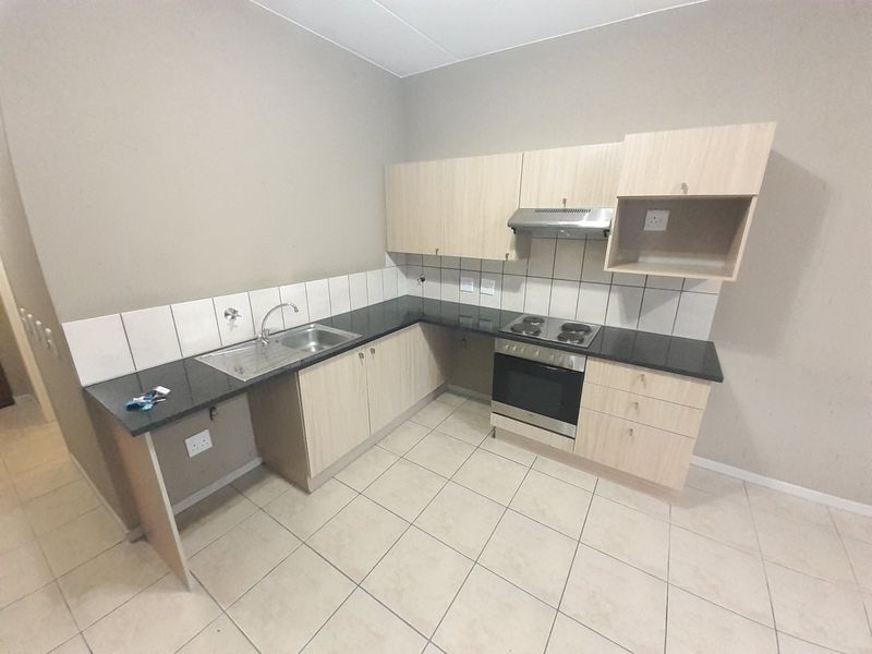 A functional kitchen featuring light wood-finish cabinetry, granite countertops, built-in oven, hob, and extractor fan with neutral tiled flooring.