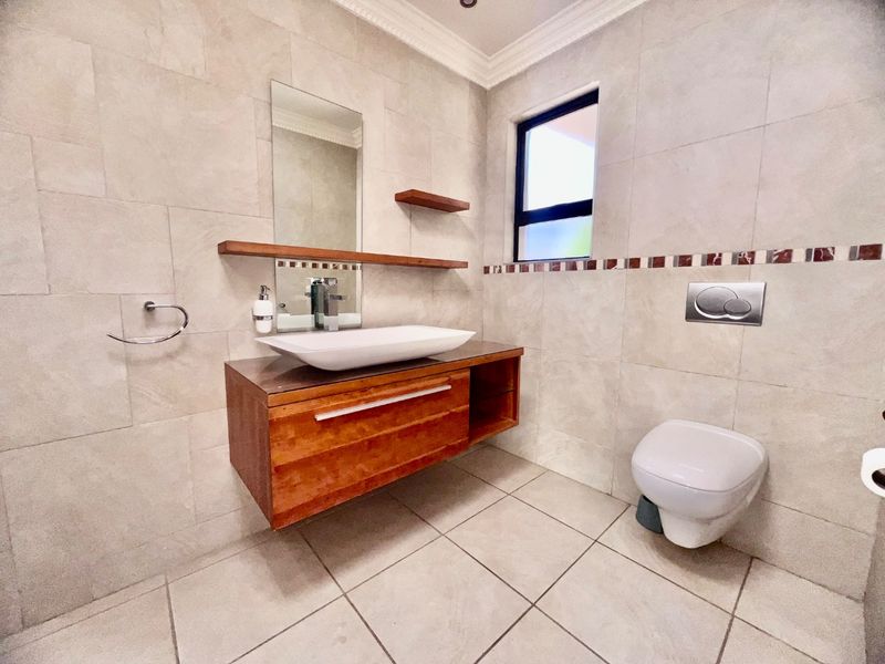 Modern bathroom featuring a wall-mounted wooden vanity with a vessel sink, wall-hung toilet, and neutral floor-to-ceiling tiling.
