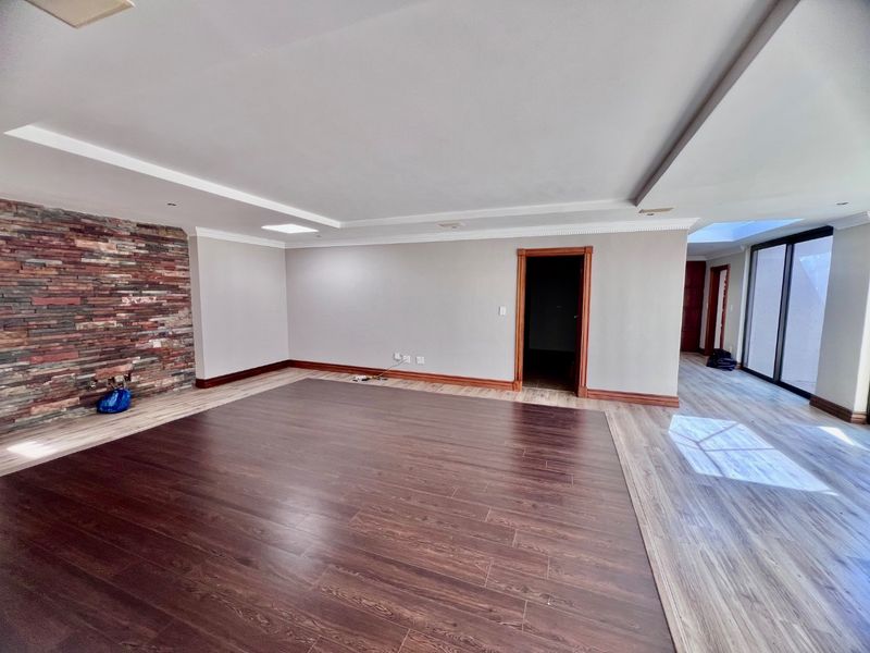 Spacious living area featuring a stone accent wall, dual-tone laminate flooring, recessed ceiling details, and large sliding doors leading to an outdoor space.