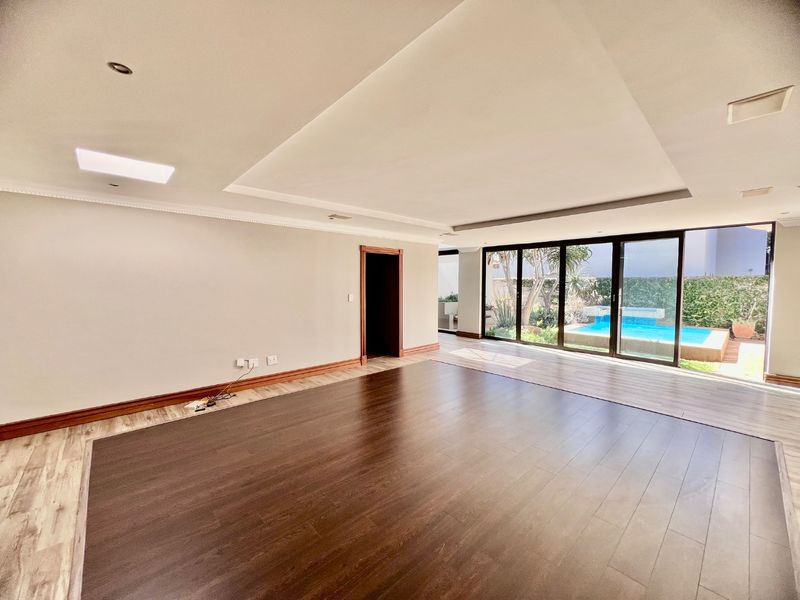 Spacious, light-filled living area featuring modern laminate flooring, recessed ceiling details, and large sliding glass doors opening onto a private pool area.