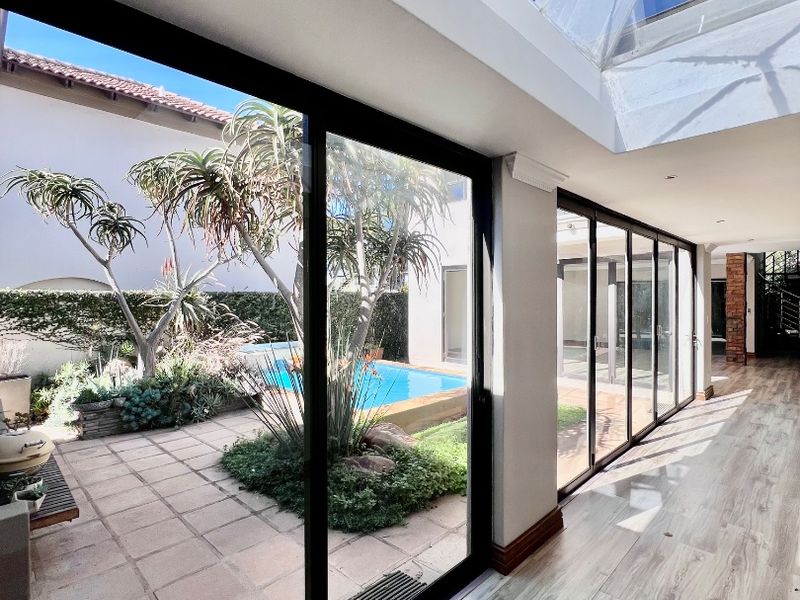 A bright, modern indoor-outdoor transition space featuring a large skylight, wood-look tiled flooring, and expansive sliding glass doors overlooking the pool and garden area.