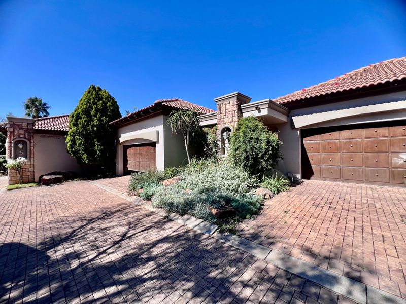 Front elevation of a well-maintained house featuring a paved driveway, double garage, stone-clad accents, and established garden landscaping.