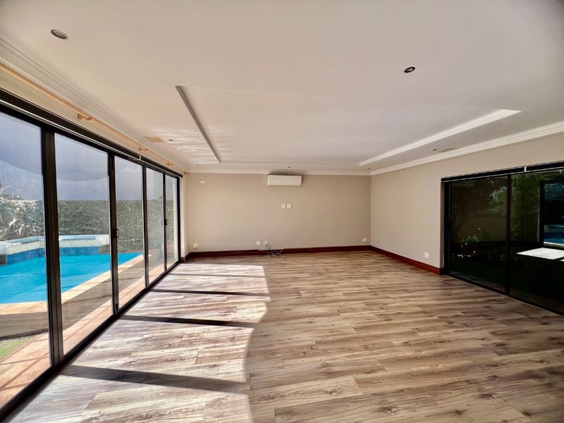 Spacious, light-filled living area featuring modern laminate flooring, recessed lighting, and large sliding glass doors providing direct access to the pool area.