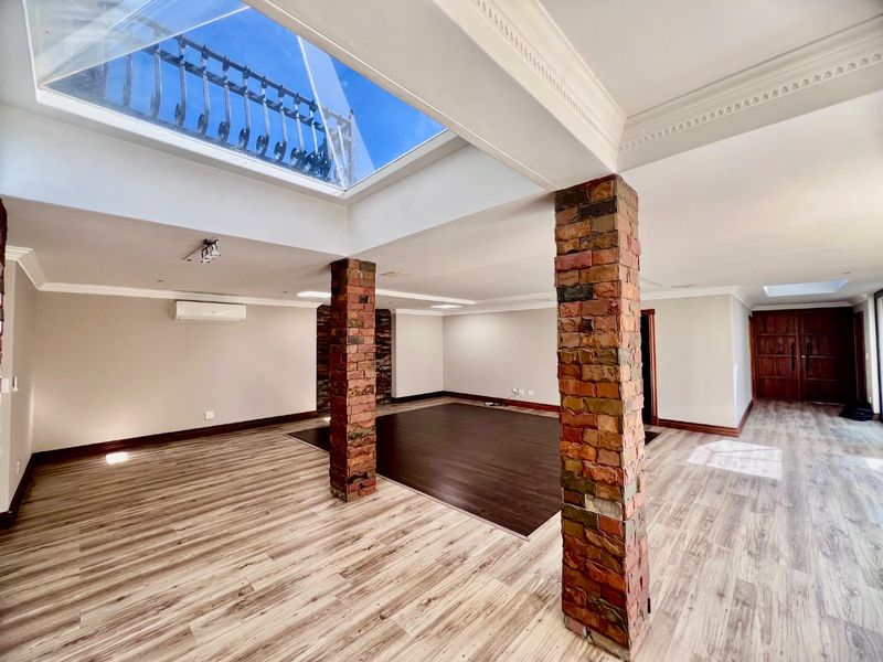 Spacious open-plan living area featuring exposed brick columns, modern laminate flooring, crown molding, and a large skylight providing abundant natural light.