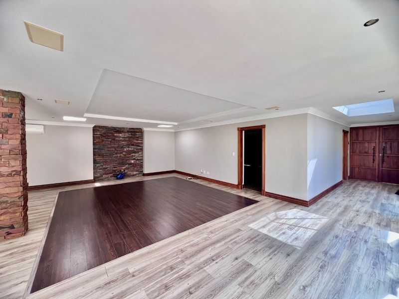 Spacious living area featuring a stone accent wall, recessed ceiling detail, skylight, and contrasting dark and light wood-look flooring.