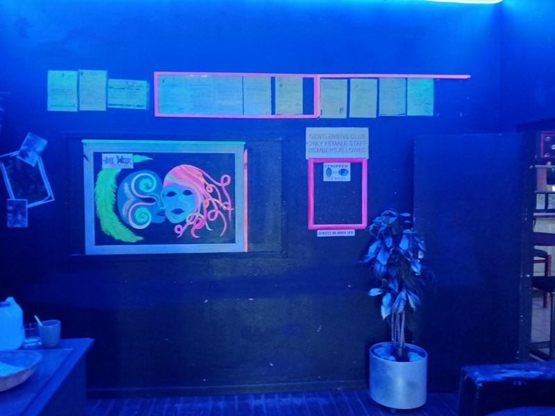 Interior space with dark walls, neon lighting, and various signage displayed on the wall.