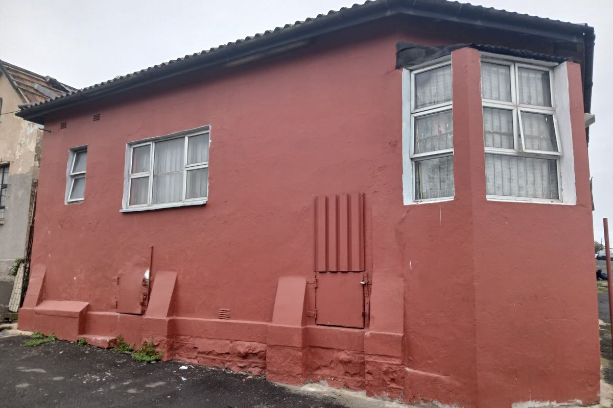 Exterior view of a residential building featuring a red plastered facade, bay window, and tiled roof, showing signs of wear and weathering.