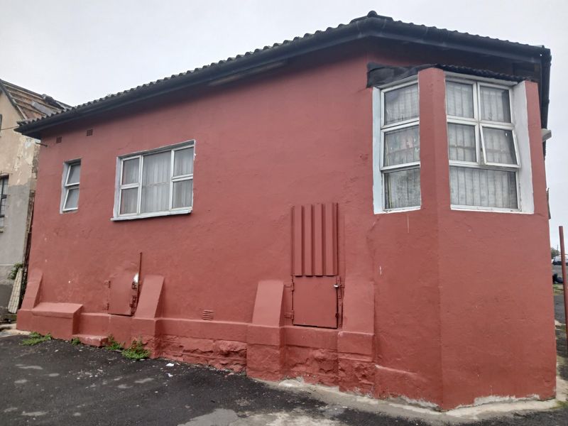 Exterior view of a residential building featuring a red plastered facade, bay window, and tiled roof, showing signs of wear and weathering.
