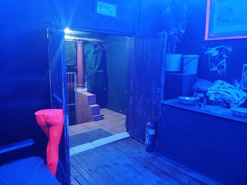 An interior space with blue lighting, featuring double wooden doors, an exit sign, and a fire extinguisher.