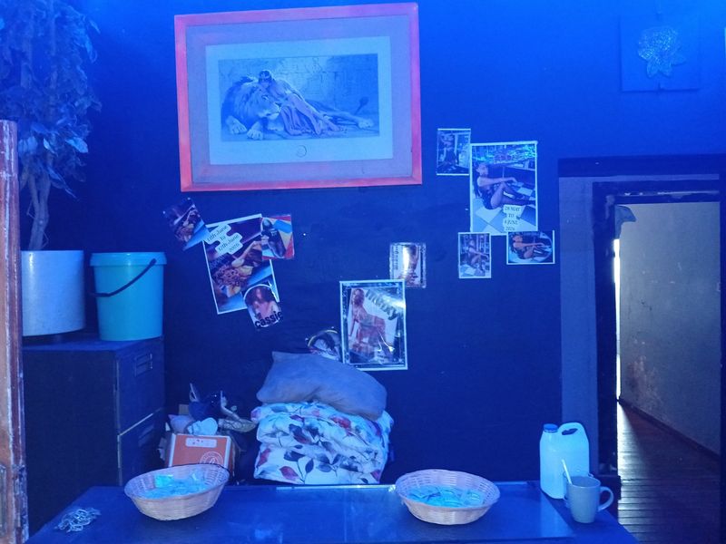 An interior space with dark blue walls, visible wall damage, and cluttered surfaces, illuminated by strong blue lighting.