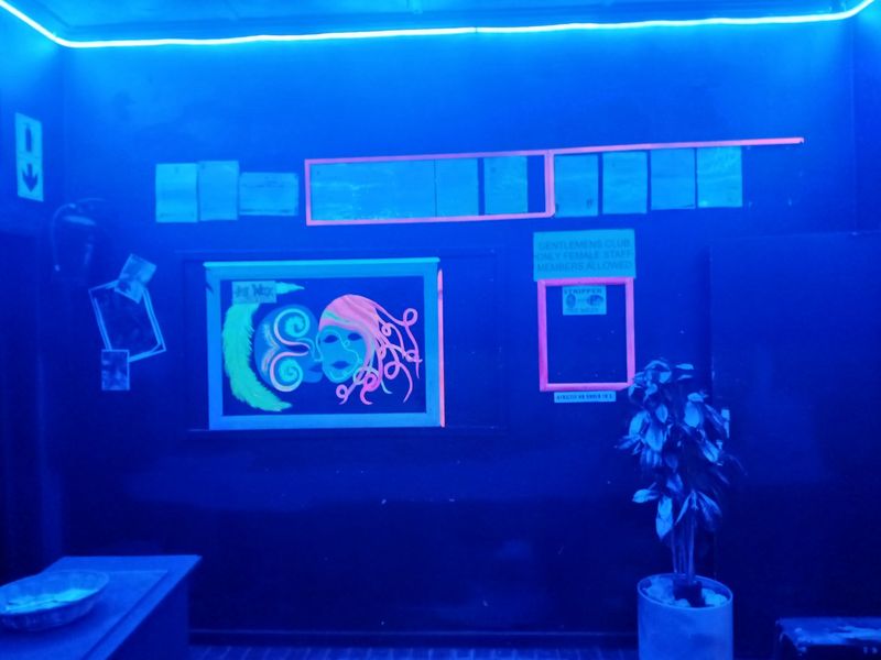An interior space featuring dark walls illuminated by blue neon lighting, with signage and decorative wall art.