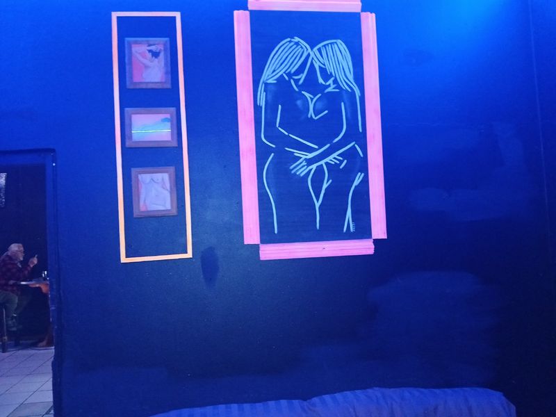An interior space featuring dark blue walls decorated with framed artwork, illuminated by blue ambient lighting.